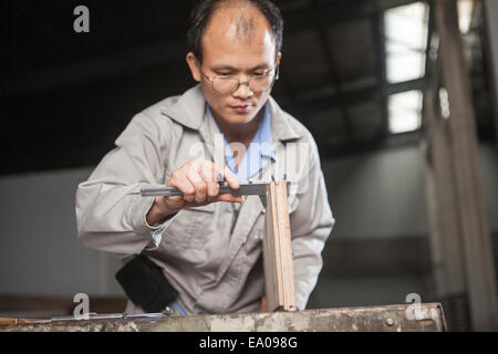 Carpenter measuring planche en bois avec pied à coulisse en usine, Jiangsu, Chine Banque D'Images