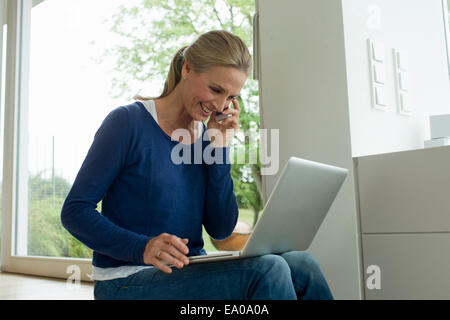 Mature Woman using laptop on cell phone Banque D'Images