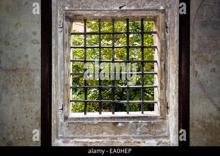 Fenêtre médiévale avec fer à repasser grille dans Prague. Les murs de pierre ancienne, cadre en bois et une vue sur les arbres Banque D'Images