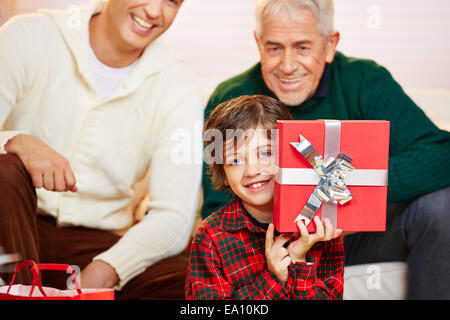 Happ boy showing red cadeau à Noël avec papa et grand-père de regarder Banque D'Images