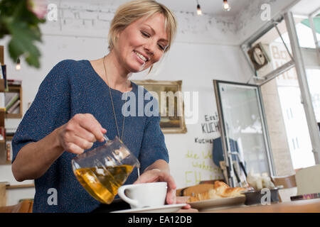 Mid adult woman pouring tea in cafe Banque D'Images