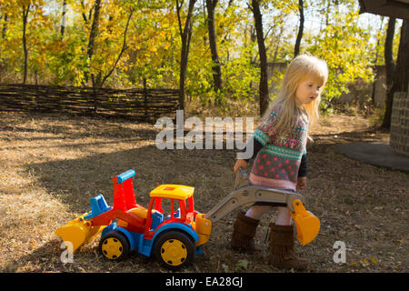 Petite fille jouant avec un jouet en plastique coloré couleurs véhicule à l'extérieur de la construction dans le parc à l'automne Sunshine Banque D'Images