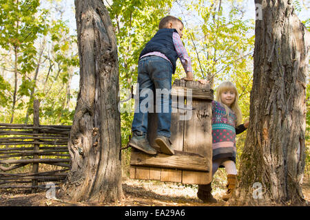 Petit garçon et fille jouant sur une ancienne porte rustique en bois entre deux arbres comme ils jouissent d'un jour à l'extérieur dans les régions rurales de Woodland Banque D'Images