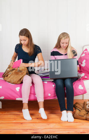 Deux teengirls assis sur le lit faisant devoirs ensemble avec les livres scolaires et l'ordinateur portable Banque D'Images