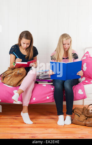 Deux teengirls assis sur le lit faisant devoirs ensemble Banque D'Images