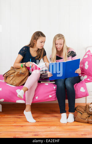 Deux teengirls assis sur le lit faisant devoirs ensemble Banque D'Images