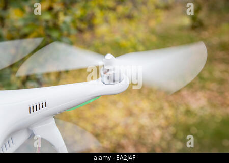 Les hélices en rotation floue d'un petit drone hélicoptère (quadcopter) survolant cour avec des feuilles sèches Banque D'Images