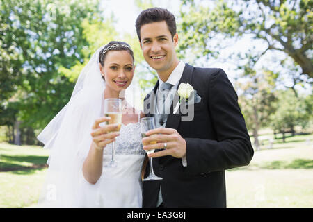 Newlywed couple toasting with champagne in park Banque D'Images