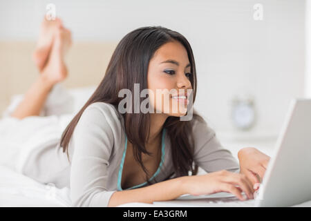 Pretty girl lying on bed using her laptop Banque D'Images