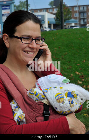 Un rire mère portant un bébé et l'aide d'un téléphone mobile Banque D'Images