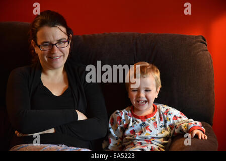 Mère et fils en pyjama, assis sur un canapé rire ensemble Banque D'Images