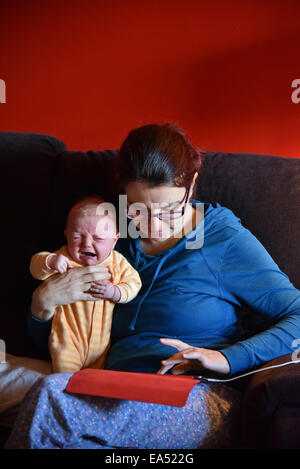 Une mère en pyjama à l'aide d'un ipad et d'ignorer son bébé qui pleure Banque D'Images