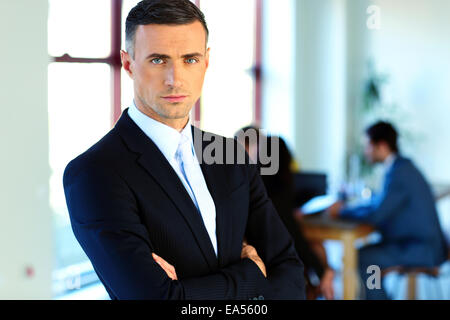 Serious businessman standing with arms folded devant des collègues Banque D'Images