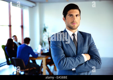 Serious businessman standing with arms folded devant des collègues Banque D'Images