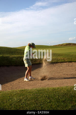 Un golfeur professionnel femme frapper sa balle d'un bunker avec le sable et la balle en l'air Banque D'Images