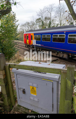 East Midlands train passant sur un sentier public avec panneau d'avertissement et d'une boîte de distribution électrique gris. Banque D'Images