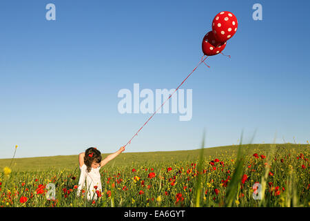 Girl standing dans un champ de fleurs de pavot à pois holding balloons Banque D'Images