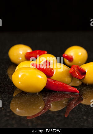 Green olives farcies aux piments rouges dans l'huile d'olive sur un plan de travail en granit noir réfléchissante Banque D'Images