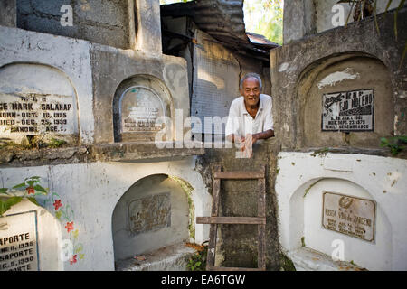 Un vieil homme de son pays fait son accueil parmi les tombes d'un cimetière de béton à Bacolod City. Banque D'Images