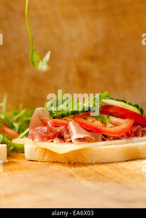 Feuilles de roquettes (motion blur), relevant de l'ouverture de sandwich pain Bloomer blanc jambon prosciutto, fromage gruyère, tomate et concombre sl Banque D'Images