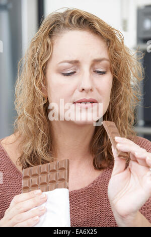 Femme coupable sur le régime alimentaire de manger une barre de chocolat à la maison Banque D'Images