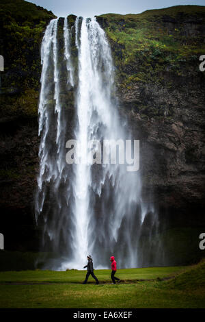 Cascade de Skogafoss dans le sud-ouest de l'Islande avec deux touristes marcher devant elle Banque D'Images