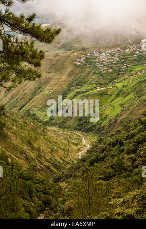 Un petit village est perché sur le bord d'une pente raide sous les nuages brumeux dans la cordillère des montagnes de Baguio, Philippines. Banque D'Images