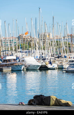 Un pauvre homme étendu sur le sol en face de Port Vell à Barcelone, Catalogne, Espagne Banque D'Images