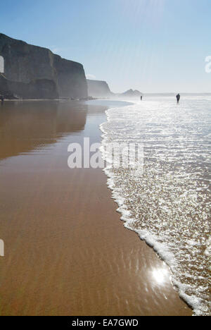 Tourné vers le soleil de promeneurs sur bord de l'eau sur la plage à marée basse le Watergate Bay sur la côte nord des Cornouailles près de sw Banque D'Images