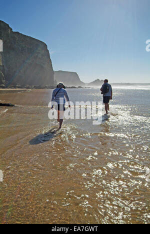 Tourné vers le soleil de promeneurs sur bord de l'eau sur la plage à marée basse le Watergate Bay sur la côte nord des Cornouailles près de sw Banque D'Images