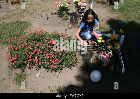 Palo, Philippines. Nov 8, 2014. Une jeune fille s'allume une bougie sur une tombe de fortune recouvert d'une lutte contre les mauvaises herbes en fleurs à San Joaquin, Palo, Leyte. San Joaquin à Palo, Leyte est l'un de la région la plus durement touchée par le typhon Haiyan, il y a un an. Avec les ondes de tempête aurait été d'atteindre 20 pieds, des centaines de personnes sont mortes au cours de la première heure de la tempête. Crédit : J Gerard Seguia/Pacific Press/Alamy Live News Banque D'Images