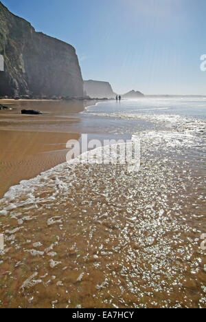 Tourné vers le soleil de promeneurs sur bord de l'eau sur la plage à marée basse le Watergate Bay sur la côte nord des Cornouailles près de sw Banque D'Images