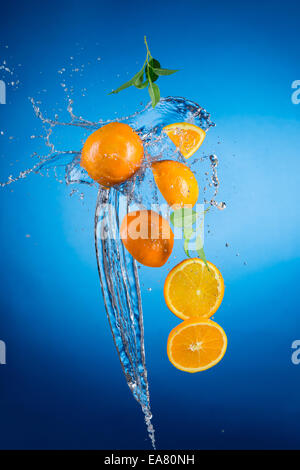 Portrait d'oranges fraîches avec de l'eau splash sur fond bleu Banque D'Images