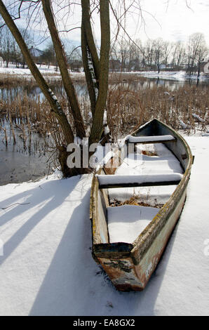 Vieux bateau en bois sur le lac rivière côte recouverte de neige en hiver Banque D'Images