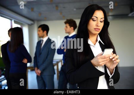 Beautiful woman using smartphone avec des collègues à l'arrière-plan Banque D'Images