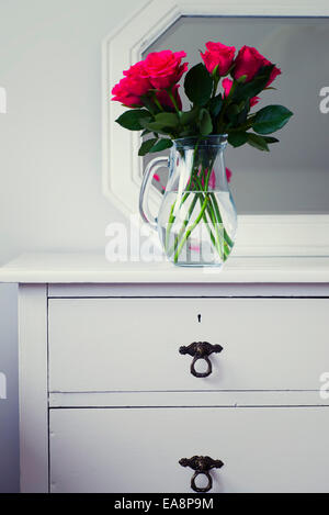 Cerise roses dans un vase en verre sur shabby chic en bois blanc commode avec miroir derrière Banque D'Images