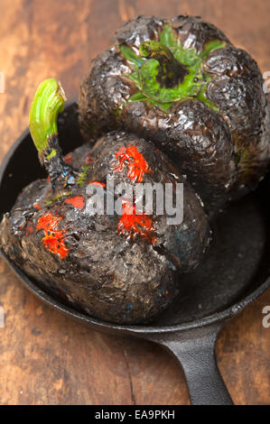 Trois poivrons frais charcol scorched sur vieux bois table sur un skillett Banque D'Images