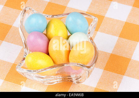 Close-up de quelques oeufs en chocolat enrobées de sucre dans un bol en verre, sur un fond jaune et blanc. Banque D'Images