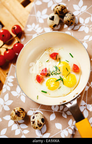 Petit-déjeuner frais avec les œufs au plat. Oeufs de caille dans un peu jaune poêle, tomates cerise servi sur table en bois. Vue d'en haut. Banque D'Images
