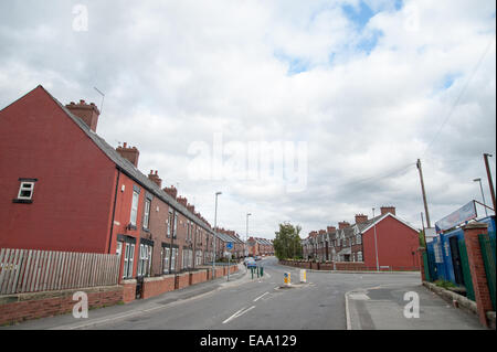 Rue résidentielle calme bordée de maisons mitoyennes traditionnelles en briques rouges dans une ville du nord du Royaume-Uni sous un ciel nuageux Banque D'Images