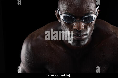 Portrait d'un jeune homme africain portant des lunettes de natation isolé sur fond noir. Mettre en place jeune athlète. Banque D'Images