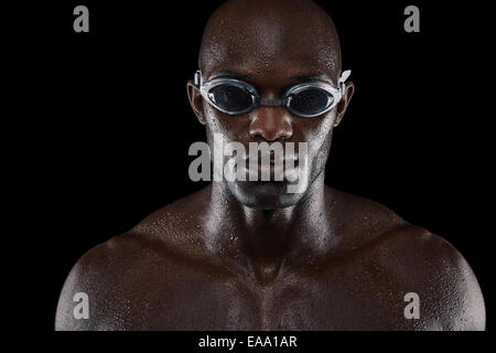 Portrait of smiling at camera nageur sur fond noir. Close-up image of muscular young man wearing swim Banque D'Images