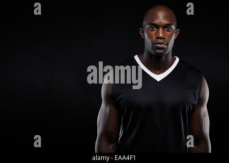 Portrait of muscular young man in sportswear looking at camera sur fond noir. Les pays africains avec l'athlète copyspace Banque D'Images