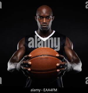 Portrait de jeune homme musclé avec un joueur de basket-ball Basket-ball posant sur fond noir. L'afro-américain de l'athlète masculin. Banque D'Images