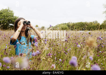 A girl holding jumelles, un jeune oiseau watcher dans un pré de hautes herbes et de fleurs sauvages. Banque D'Images