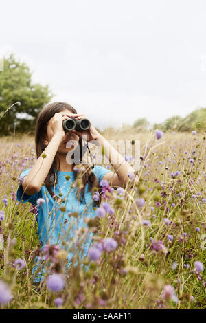 A girl holding jumelles, un jeune oiseau watcher dans un pré de hautes herbes et de fleurs sauvages. Banque D'Images