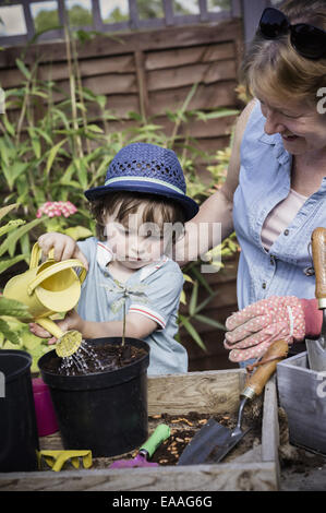 Une femme et un jeune enfant eau nouveau graines semées dans un pot. Banque D'Images