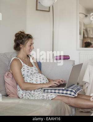 Une femme enceinte assise sur sur un canapé avec ses pieds. Banque D'Images