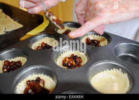 Femme âgée mince pies de cuisson pensionné à la maison dans sa cuisine pour Noël . Mettre la viande hachée dans les coquilles de pâtisserie Banque D'Images