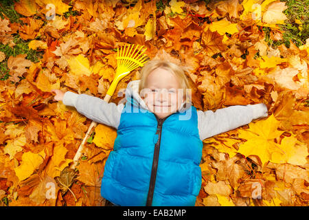 Heureux garçon blond portant sur les feuilles d'automne Banque D'Images